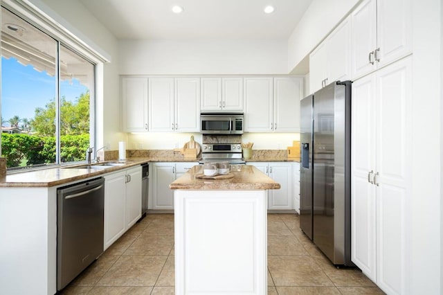 kitchen with a center island, sink, light tile patterned floors, appliances with stainless steel finishes, and white cabinetry