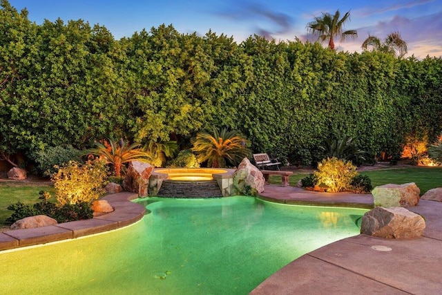 pool at dusk featuring an in ground hot tub