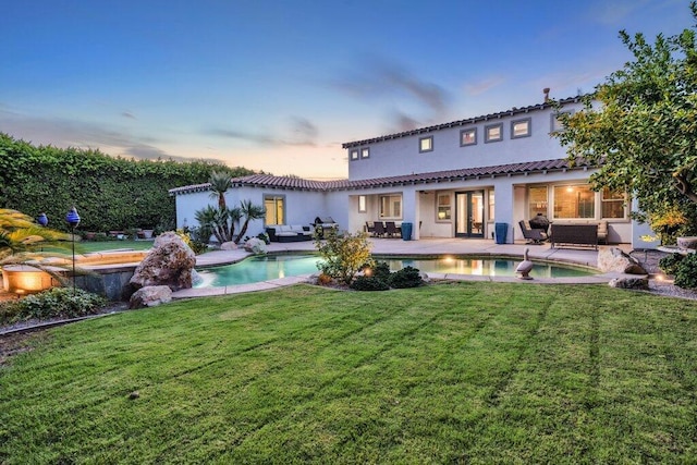 back house at dusk featuring a lawn and an outdoor hangout area