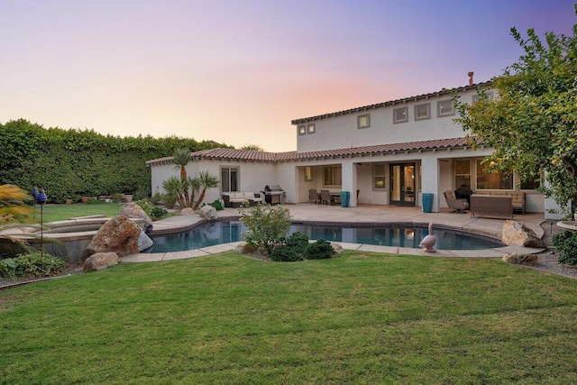 back house at dusk featuring outdoor lounge area, a patio area, and a lawn