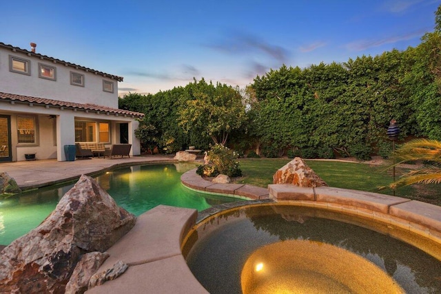 pool at dusk with an in ground hot tub and a yard