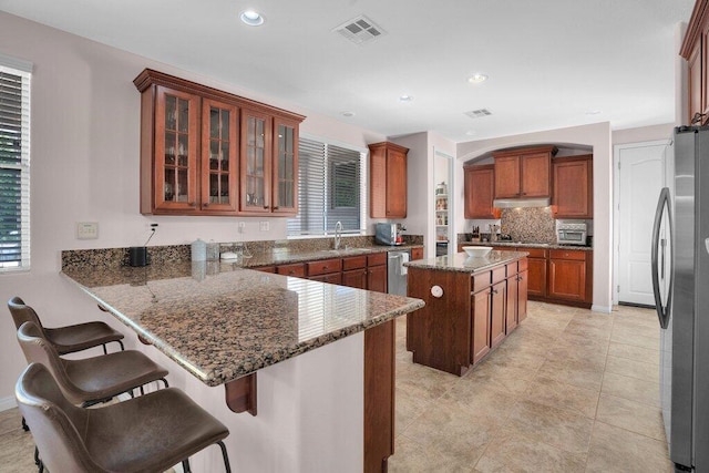 kitchen with stainless steel appliances, kitchen peninsula, dark stone countertops, a breakfast bar, and a kitchen island