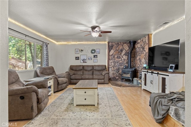 living room featuring ceiling fan, a textured ceiling, light wood-type flooring, and a wood stove