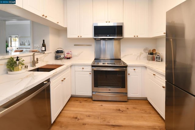 kitchen with light stone countertops, sink, stainless steel appliances, light hardwood / wood-style floors, and white cabinets