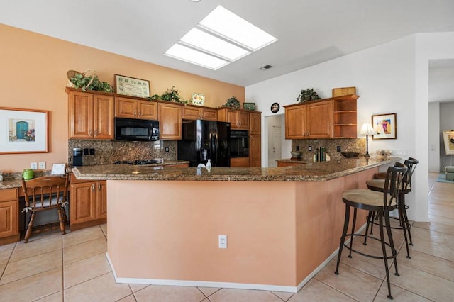 kitchen featuring black appliances, kitchen peninsula, a kitchen bar, and tasteful backsplash