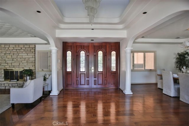 entrance foyer featuring a chandelier, dark hardwood / wood-style flooring, a raised ceiling, and a stone fireplace