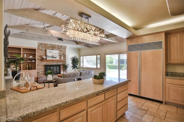 kitchen featuring paneled refrigerator, light stone counters, beam ceiling, an inviting chandelier, and a fireplace