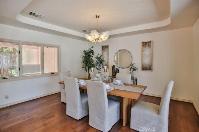 dining space featuring dark hardwood / wood-style floors, an inviting chandelier, and a tray ceiling