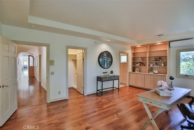 home office with wood-type flooring, an AC wall unit, and a raised ceiling