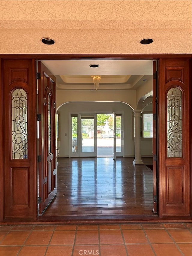 foyer featuring wood-type flooring, a textured ceiling, and ornate columns