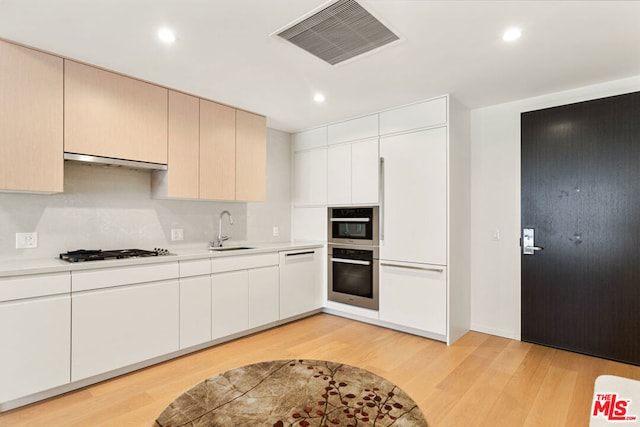 kitchen with extractor fan, sink, light hardwood / wood-style floors, white cabinetry, and stainless steel gas stovetop