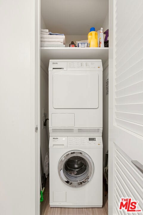 clothes washing area with light hardwood / wood-style flooring and stacked washer and clothes dryer