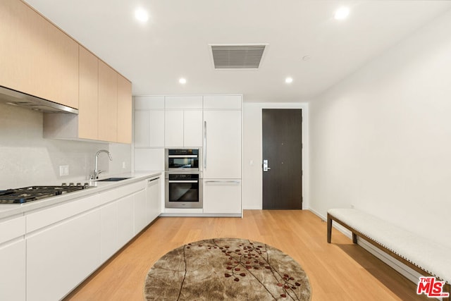 kitchen with white cabinetry, sink, stainless steel appliances, and light hardwood / wood-style flooring