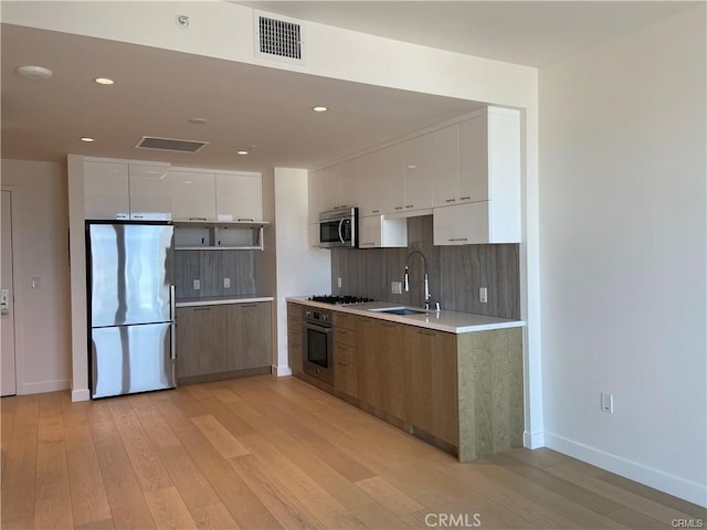 kitchen featuring white cabinets, sink, tasteful backsplash, appliances with stainless steel finishes, and light hardwood / wood-style floors