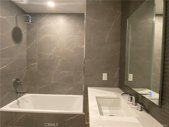 bathroom with tiled shower / bath, vanity, and tile walls