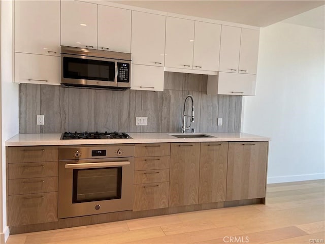 kitchen with appliances with stainless steel finishes, backsplash, sink, and light hardwood / wood-style flooring