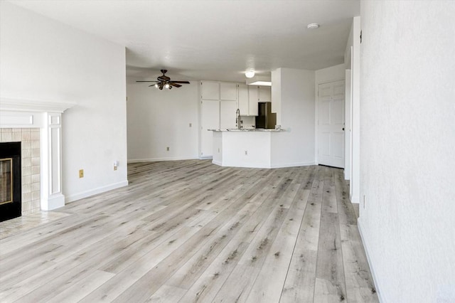 unfurnished living room featuring light wood finished floors, ceiling fan, baseboards, and a tile fireplace