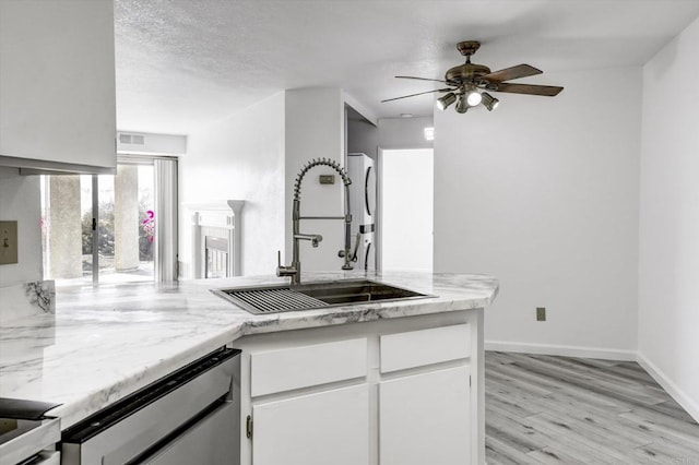 kitchen with a sink, visible vents, white cabinets, stainless steel dishwasher, and light wood-type flooring