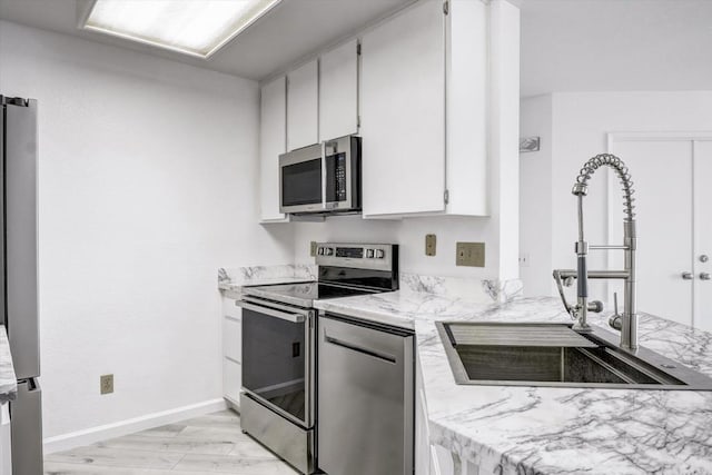 kitchen featuring light wood finished floors, baseboards, appliances with stainless steel finishes, white cabinetry, and a sink