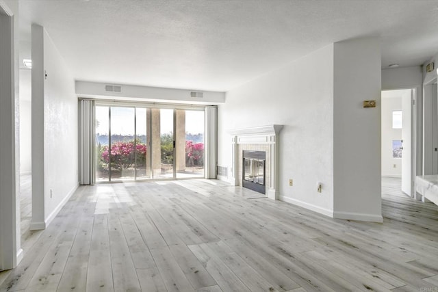 unfurnished living room with light wood-type flooring, baseboards, a fireplace, and visible vents