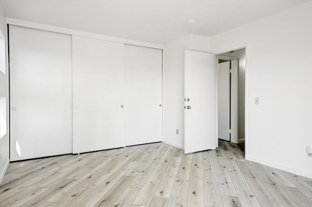 unfurnished bedroom featuring a closet, light wood-style flooring, and baseboards