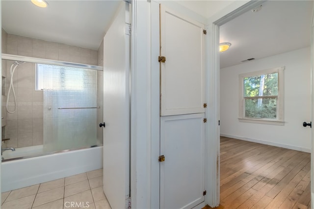 bathroom with a wealth of natural light, shower / bath combination with glass door, and hardwood / wood-style flooring