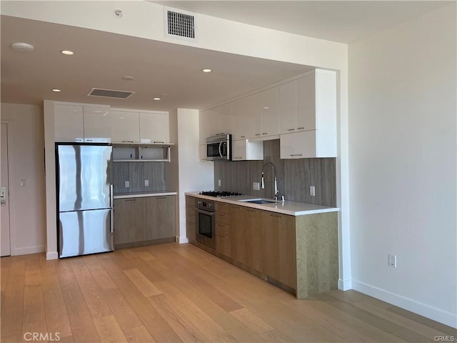 kitchen featuring appliances with stainless steel finishes, light hardwood / wood-style floors, sink, and white cabinets