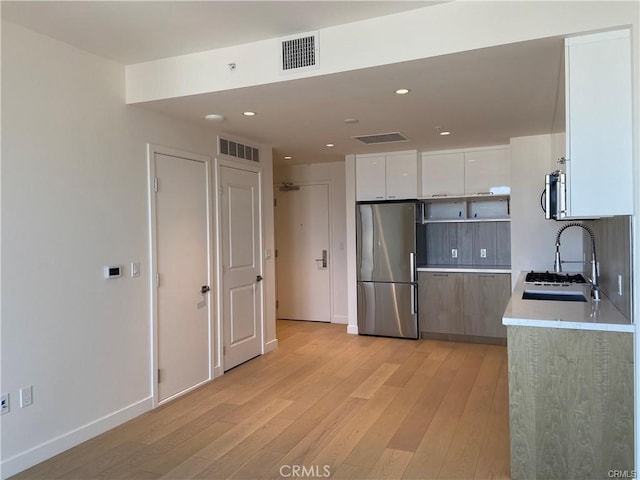 kitchen featuring tasteful backsplash, sink, white cabinets, light hardwood / wood-style flooring, and stainless steel appliances