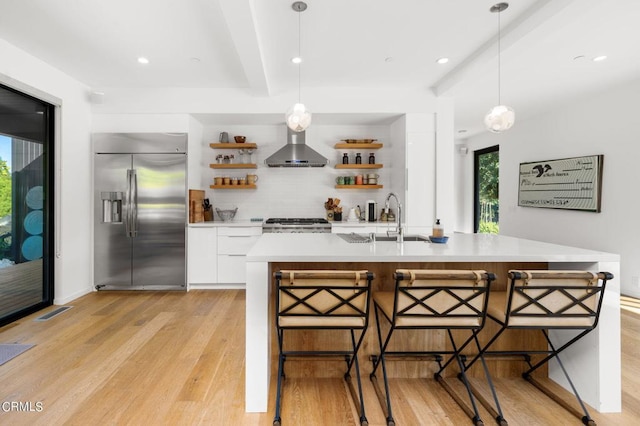 kitchen with appliances with stainless steel finishes, white cabinetry, a wealth of natural light, and wall chimney exhaust hood