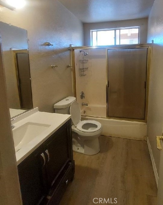 full bathroom featuring shower / bath combination with glass door, vanity, hardwood / wood-style floors, and toilet