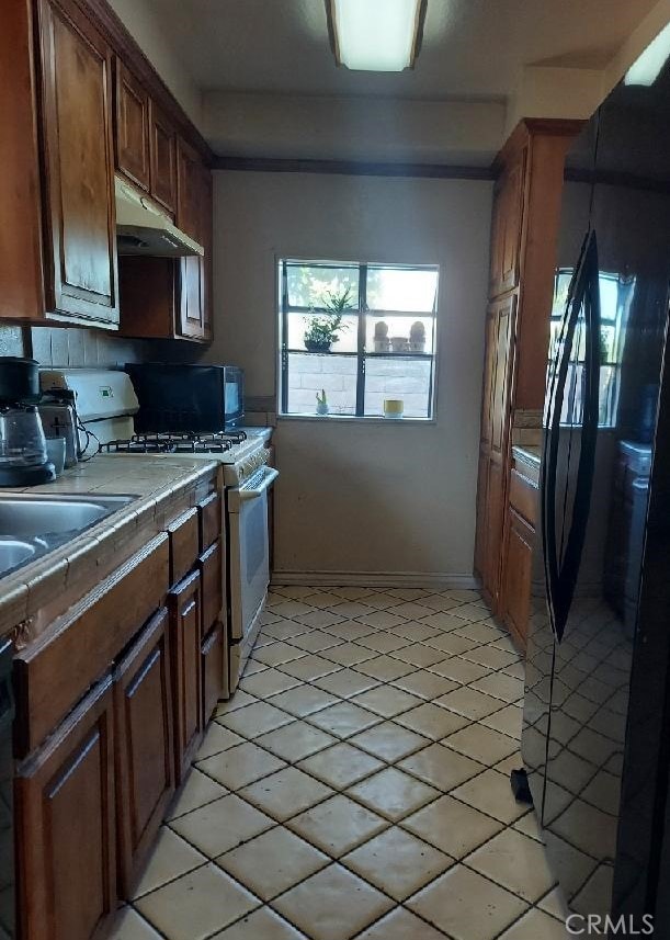 kitchen featuring black fridge, tile countertops, light tile patterned floors, and white gas range