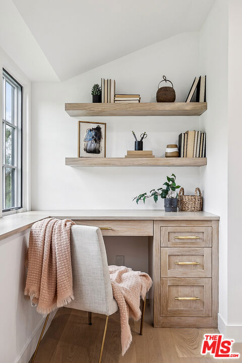 interior space with built in desk, light hardwood / wood-style flooring, and vaulted ceiling