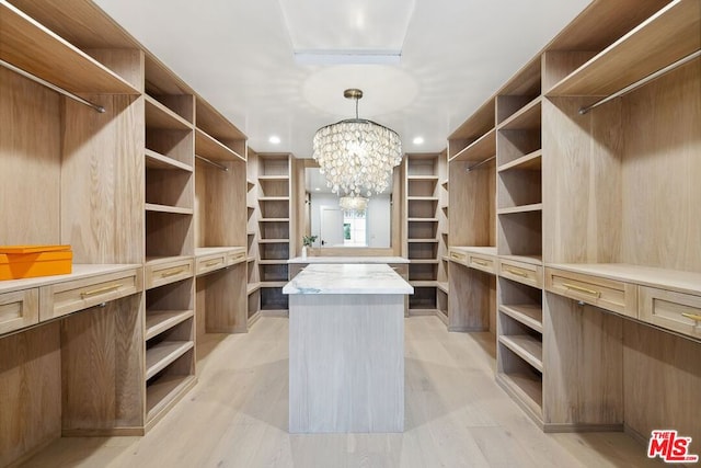 spacious closet featuring light wood-type flooring and an inviting chandelier