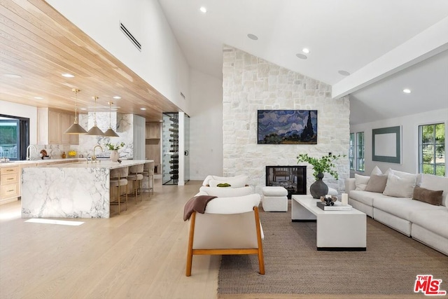 living room featuring light hardwood / wood-style floors, a stone fireplace, sink, and vaulted ceiling