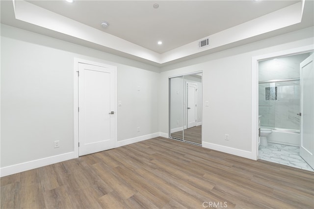 unfurnished bedroom with connected bathroom, hardwood / wood-style floors, and a closet