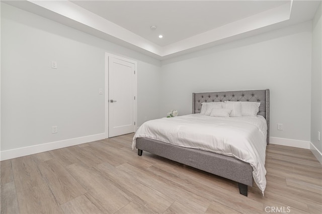 bedroom with light hardwood / wood-style flooring and a raised ceiling