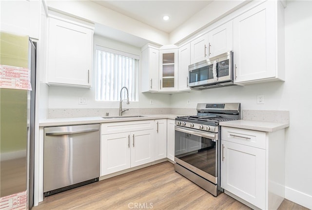 kitchen featuring stainless steel appliances, white cabinets, light wood-type flooring, and sink