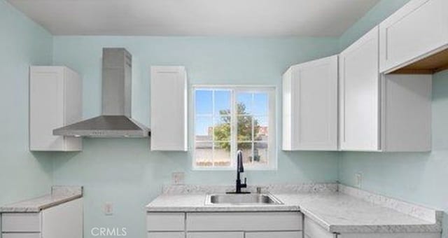 kitchen featuring white cabinetry, wall chimney range hood, and sink