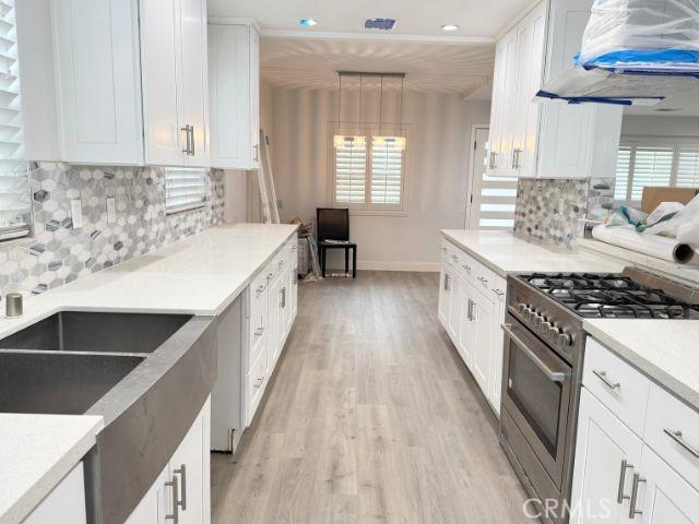 6053 Turnergrove Dr, Lakewood, CA 90713 - kitchen featuring high end range, light wood finished floors, white cabinetry, wall chimney range hood, and recessed lighting