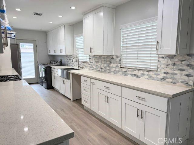 6053 Turnergrove Dr, Lakewood, CA 90713 - kitchen with a sink, washing machine and clothes dryer, light wood-style flooring, decorative backsplash, and white cabinets