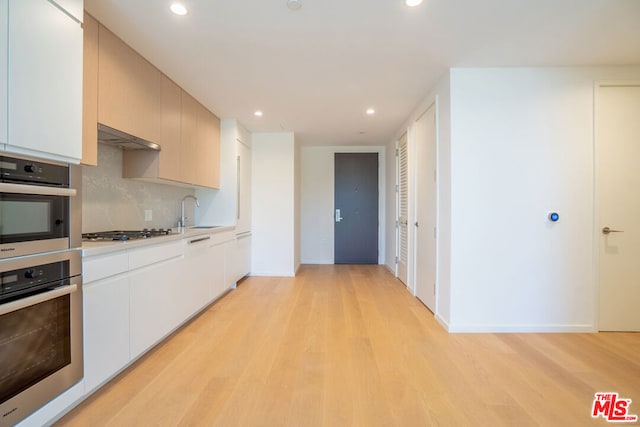 kitchen featuring white cabinets, appliances with stainless steel finishes, decorative backsplash, sink, and light wood-type flooring