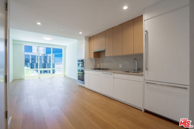 kitchen with floor to ceiling windows, stainless steel appliances, tasteful backsplash, light hardwood / wood-style flooring, and sink