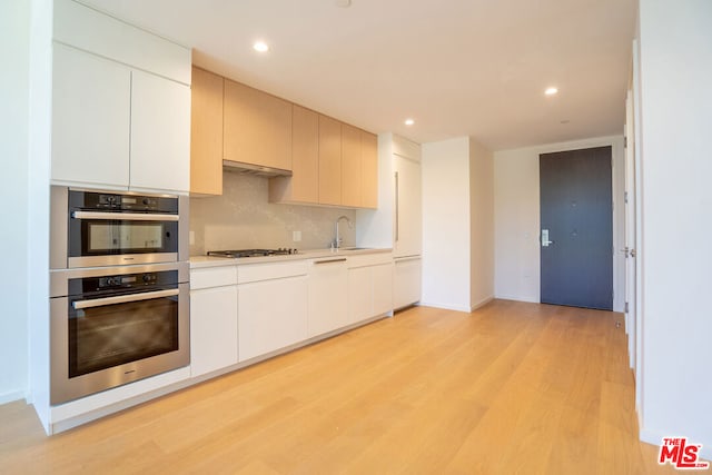 kitchen with white cabinetry, light hardwood / wood-style floors, appliances with stainless steel finishes, decorative backsplash, and sink