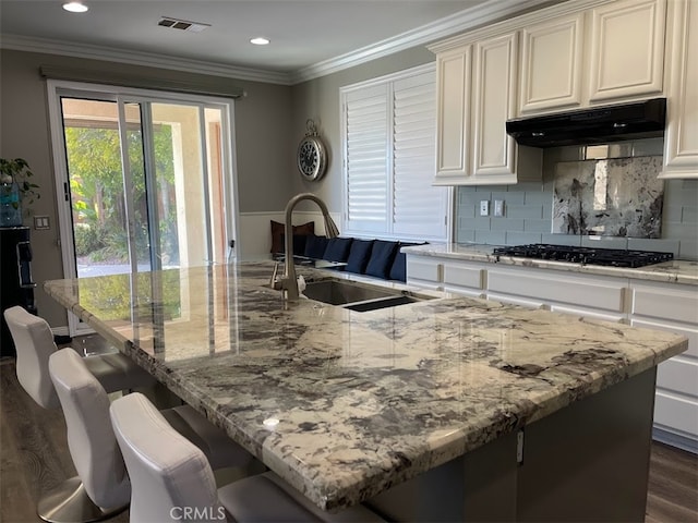 kitchen with sink, black gas cooktop, a center island with sink, dark hardwood / wood-style floors, and a breakfast bar area