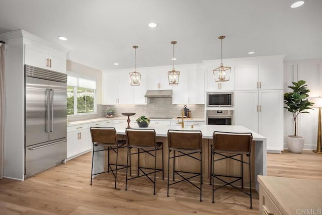 kitchen with white cabinets, under cabinet range hood, light countertops, and built in appliances