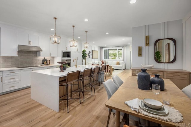 kitchen with a center island with sink, light countertops, built in microwave, under cabinet range hood, and black electric cooktop