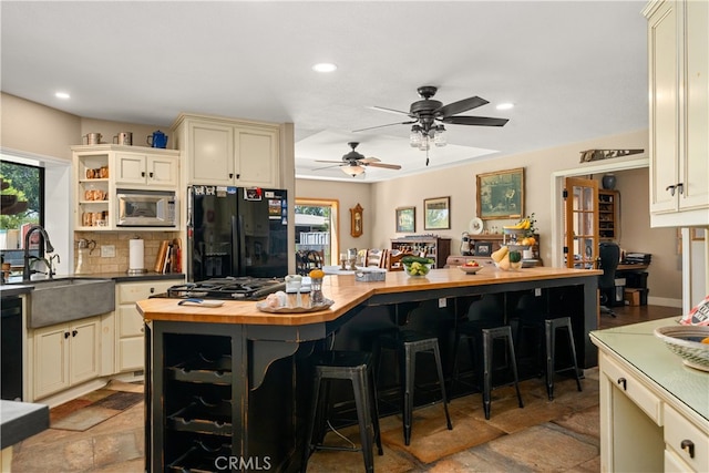 kitchen featuring cream cabinets, wooden counters, a healthy amount of sunlight, and black appliances