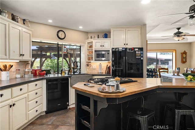 kitchen featuring black appliances, cream cabinetry, a kitchen bar, wood counters, and decorative backsplash