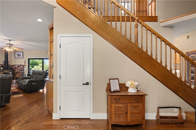 staircase with a wood stove, wood-type flooring, and ceiling fan