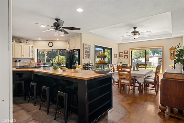 kitchen featuring a breakfast bar area, black refrigerator, a raised ceiling, and dark hardwood / wood-style flooring